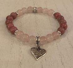 "Beautiful rose quartz and rhodonite 8mm beads are paired with a silver heart charm to create a fun to wear wrist mala for Valentines or anytime a little extra heart is needed. The bracelet is strung on 1mm Stretch Magic cord and easily rolls over your hand to rest on the wrist. I can custom make any size you need. Just select the size you need from the pull down menu or convo me with your request. To determine what size you need, use a tape measure, or if you don't have one, use a piece of stri Rose Quartz Beaded Bracelets For Valentine's Day, Pink Rose Quartz Stretch Bracelet, Pink Heart-shaped Spiritual Beaded Bracelets, Spiritual Hand-strung Rose Quartz Stretch Bracelet, Adjustable Rose Quartz Crystal Bracelet, Spiritual Style, Adjustable Rose Quartz Bracelets - Spiritual Style, Wrist Mala, 8mm Beads, Blue Tigers Eye