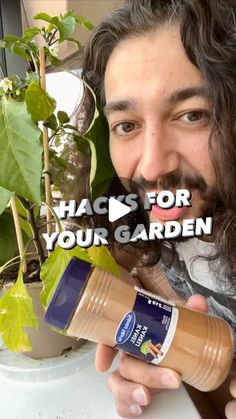 a man with long hair is holding a jar and smiling at the camera while sitting in front of a potted plant