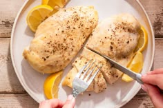 someone is cutting up some chicken on a white plate with lemons and a fork