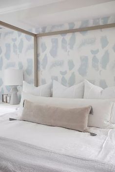 a white bed topped with pillows next to a wallpaper covered in blue and white paint