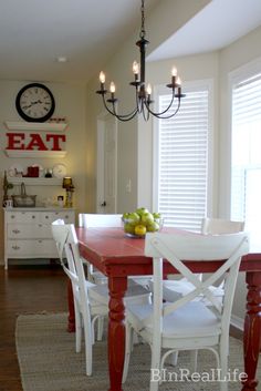 a red table with white chairs and a clock on the wall above it in a kitchen