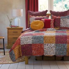 a bed with red, yellow and blue bedspread in a bedroom next to a window