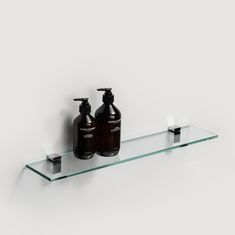 two bottles and soap dispenser on a glass shelf against a white wall