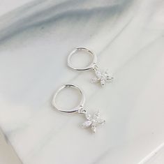 This is a pair of dainty huggie earrings which are made from 925 sterling silver and which feature a small pendant with five, clear-coloured, Marquise zircon stones arranged in a flower shape hanging from the lower edge of the hoop. They fasten with a hinge clasp (also on the lower edge of the hoop), and have a thin earpiece which threads through the earlobe. This is a delicate and elegant pair of earrings that will add a classy touch of sparkle to any outfit.  Packaging: Beautifully packed in a box, ready for gifting. Details: ✅ Material: 925 sterling silver ✅ Diameter: hoop diameter: 1.1 cm ✅ Charm size: 7.5 mm ✅ Weight: 3.0 g 🏷️ This product is made of sterling silver -- easily recognizable by its '925' stamp of authenticity. It is also hypoallergenic, making it suitable for people wit Hoops With Charms, Earrings Flower, Jewelry Lookbook, Sterling Silver Hoop Earrings, Dangly Earrings, Huggie Earrings, Small Pendant, Huggie Hoop Earrings, Sterling Silver Hoops