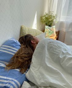 a woman laying in bed under a white and blue comforter with her head on the pillow