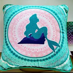 a pillow with the silhouette of a mermaid sitting on top of a blue and pink circle