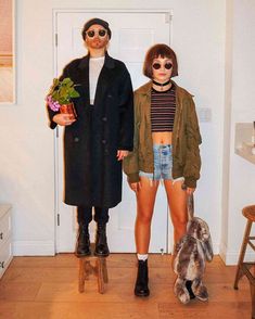 two people standing next to each other in front of a white door with a potted plant