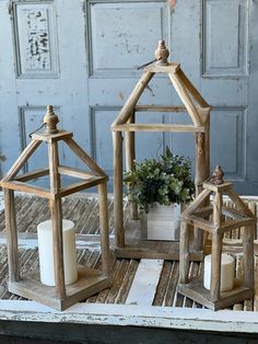 two wooden lanterns sitting on top of a table next to a white candle and potted plant