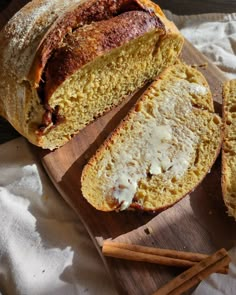 a loaf of bread sitting on top of a wooden cutting board next to cinnamon sticks