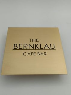 the berklauu cafe bar sign is gold and has black lettering on it