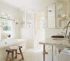 a large white bathroom with a claw foot tub and marble counter top, along with two stools in front of the bathtub