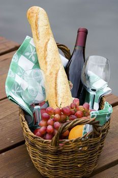 a basket filled with bread, grapes and wine on top of a wooden table next to water