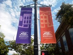 two banners are hanging from a street light pole in front of some buildings and trees