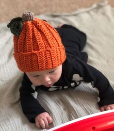 a baby wearing an orange knitted hat laying on top of a bed