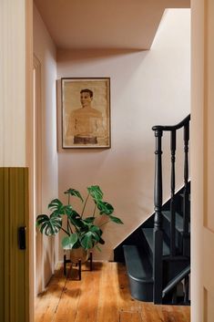 a staircase leading up to a room with a painting on the wall and a potted plant next to it