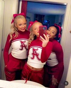 three women in red and white cheerleader outfits taking a selfie with their cell phone