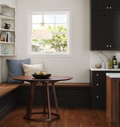 a kitchen with black cabinets and white walls, wooden flooring and a round table in front of the window