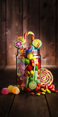 a glass jar filled with lots of candy and lollipops on top of a wooden table