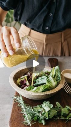 a person pouring dressing into a wooden bowl filled with lettuce and other vegetables