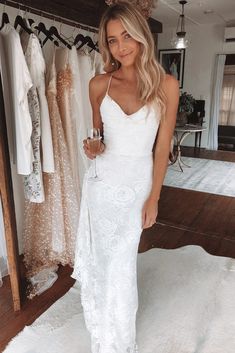 a woman wearing a white dress standing in front of a rack of wedding gowns