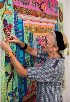 an older woman is working on a colorful piece of art that hangs on the wall