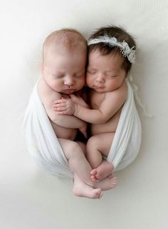 two babies are cuddling together wrapped in white cloths on a white surface with their heads touching each other