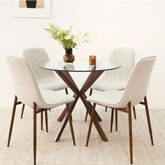 a glass table with four chairs around it and a vase on the top, in front of a white wall