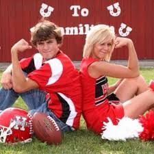 two people sitting on the grass with footballs and cheerleaders in front of them