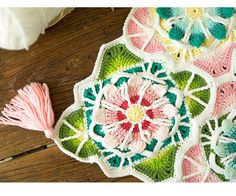 a crocheted doily with flowers and tassels on the floor next to yarn