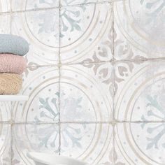 towels stacked on top of each other in front of a wall with decorative tiles behind it