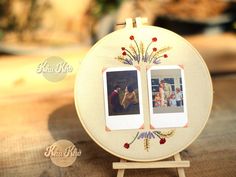 an embroidered photo frame with two pictures on it sitting on top of a wooden table