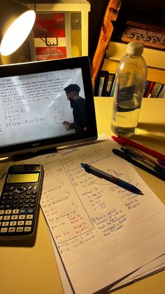 a laptop computer sitting on top of a desk next to a calculator and pen