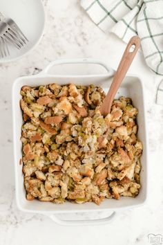 a white bowl filled with stuffing next to a wooden spoon and napkin on top of a marble counter