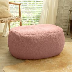 a large pink bean bag sitting on top of a wooden floor next to a window