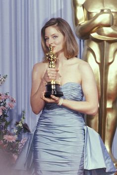 a woman holding an oscar award in front of a backdrop with flowers and a statue