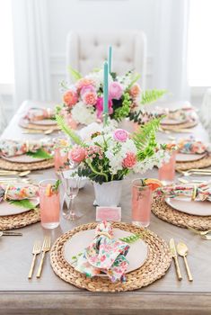 the table is set with pink and white flowers, gold place settings, and greenery