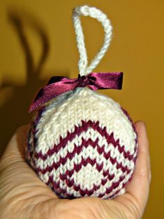 a hand holding a knitted ornament with a ribbon on it's end