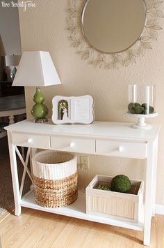 a white table with baskets and a mirror on it next to a lamp in a living room