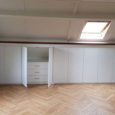 an empty room with wooden floors and white cupboards on the wall, windows in the ceiling