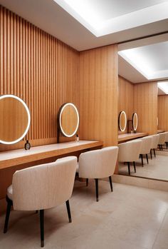 a row of white chairs sitting next to each other in front of wooden wall mounted mirrors