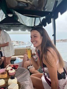 two women sitting on the back of a boat with cupcakes and drinks in front of them