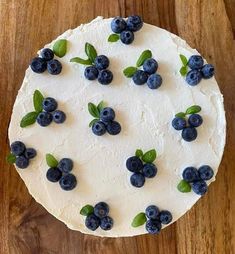 a cake with white frosting and blueberries on top sitting on a wooden table