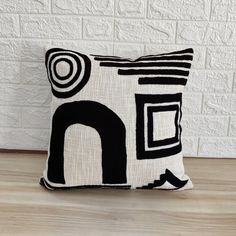 a black and white pillow sitting on top of a wooden floor next to a brick wall