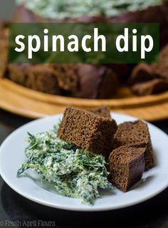 spinach dip on a white plate with brown bread and green vegetables in the background