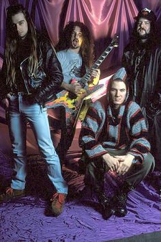 three men with long hair and beards are posing for a photo while one man is holding an electric guitar