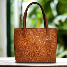 This exquisitely hand-tooled leather bag is a genuine work of art. It was carved by skilled artisans, the intricate design results in a unique and captivating piece that is guaranteed to capture attention.  Crafted from high-quality, durable leather, this hand-carved bag is built to withstand the test of time and will only grow more appealing with age. The generously sized interior is ideal for accommodating all your essentials. Whether you're off to work, running errands, or enjoying a night ou Brown Embossed Tote Shoulder Bag, Leather Shoulder Bag Engraved For Everyday Use, Engraved Leather Shoulder Bag For Everyday, Everyday Leather Shoulder Bag Engraved, Travel Hand Tooled Shoulder Bag, Traditional Leather Shoulder Bag With Embossed Detail, Elegant Engraved Shoulder Bag For Everyday Use, Leather Bag With Engraved Details For Everyday Use, Leather Bag With Engraving For Everyday Use