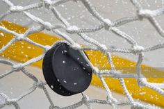 an ice hockey goalie's net with the puck stuck in it and snowing