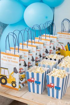 a table topped with popcorn bags filled with blue and white striped paper bags next to balloons