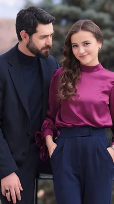 a man and woman standing next to each other in front of a tree with their hands on their hips