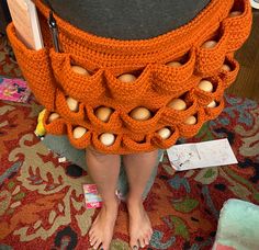 a woman is standing on the floor with her legs crossed and wearing an orange crocheted skirt